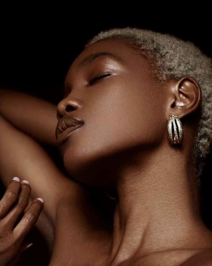 Black woman with blond hair has hand on the back of her head, neck and arm lit well, armpit visible nice makeup pretty attractice