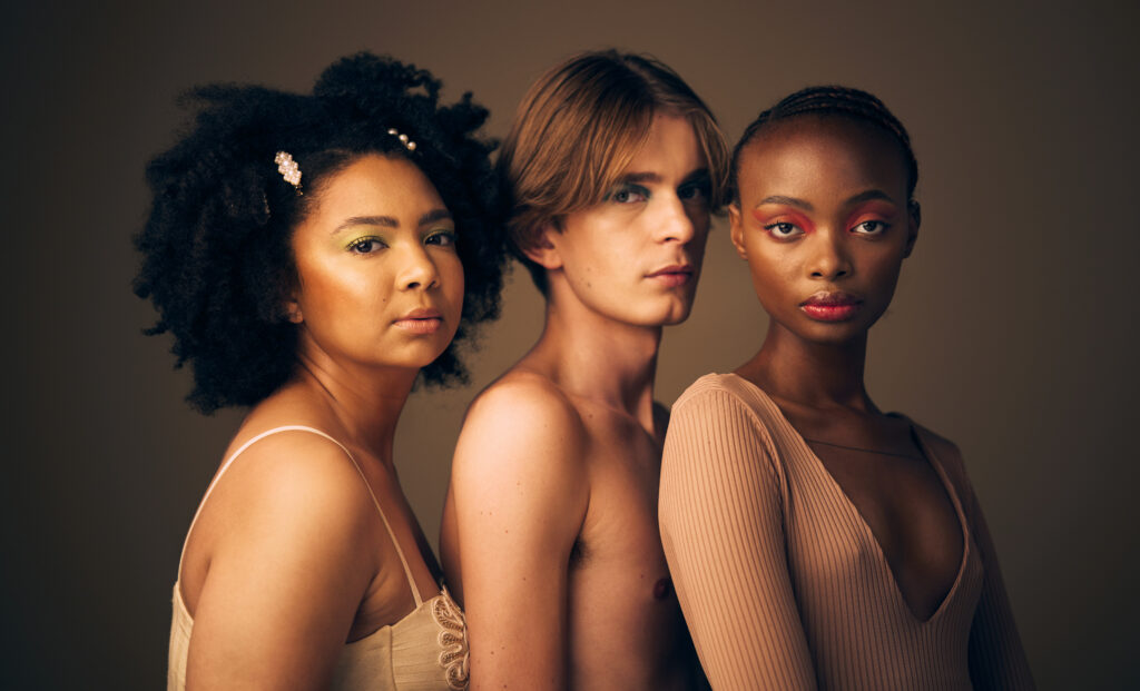 Three diverse models with creative makeup posing against a neutral studio background — inclusive beauty and fashion portrait for editorial or skincare campaign